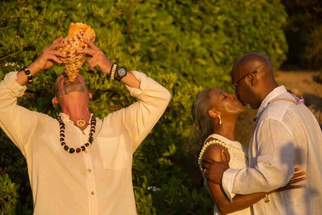 Couple sharing a kiss while man drinks from a bottle outdoors.