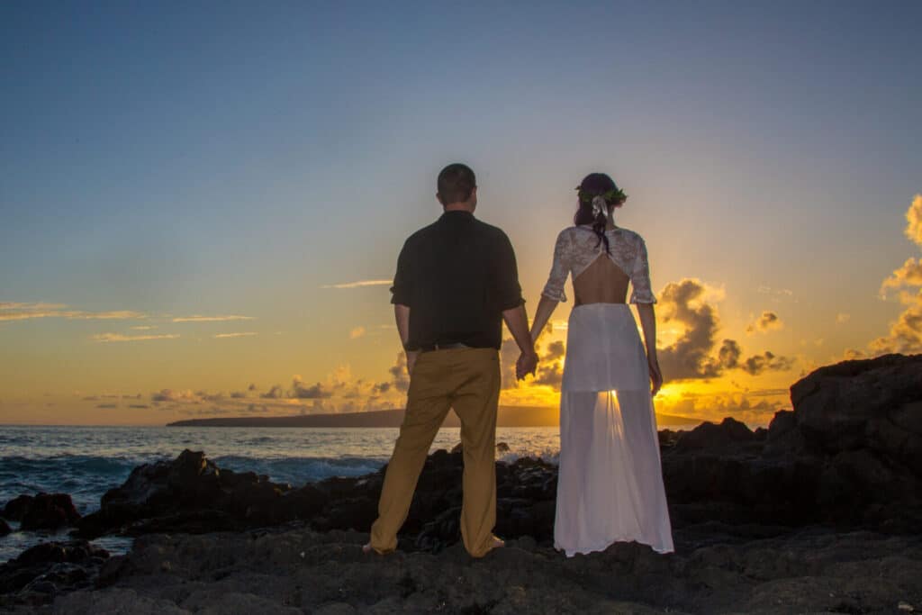 Married couple holding hands as the sunsets on a beach in Maui