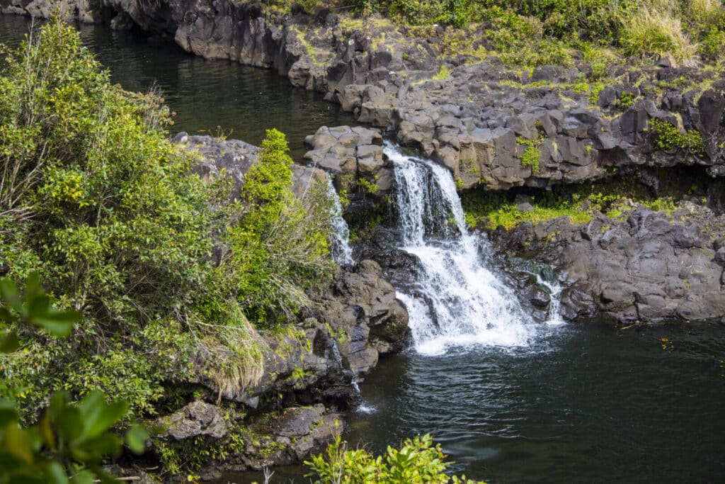 Waterfall flowing into a calm pool surrounded by rocks and greenery.