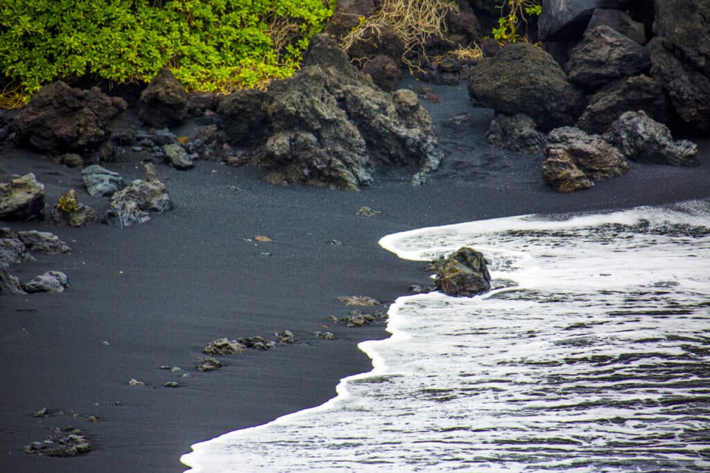 A rocky shoreline with black sand and gentle waves.