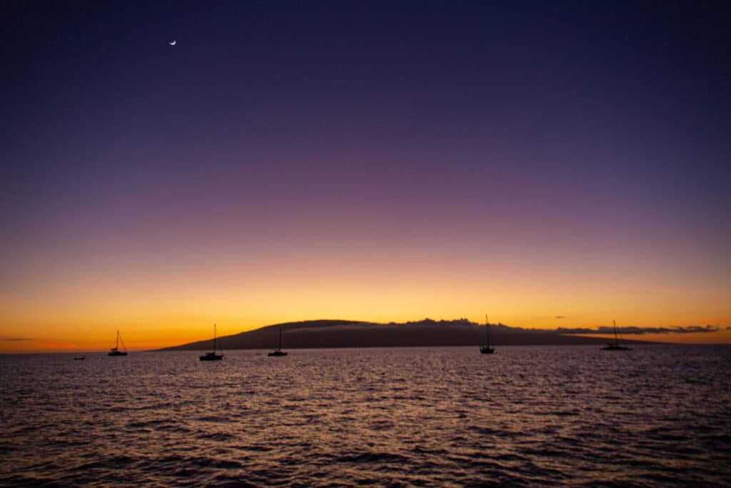 Sunset over a calm sea with a silhouetted hill in the distance.