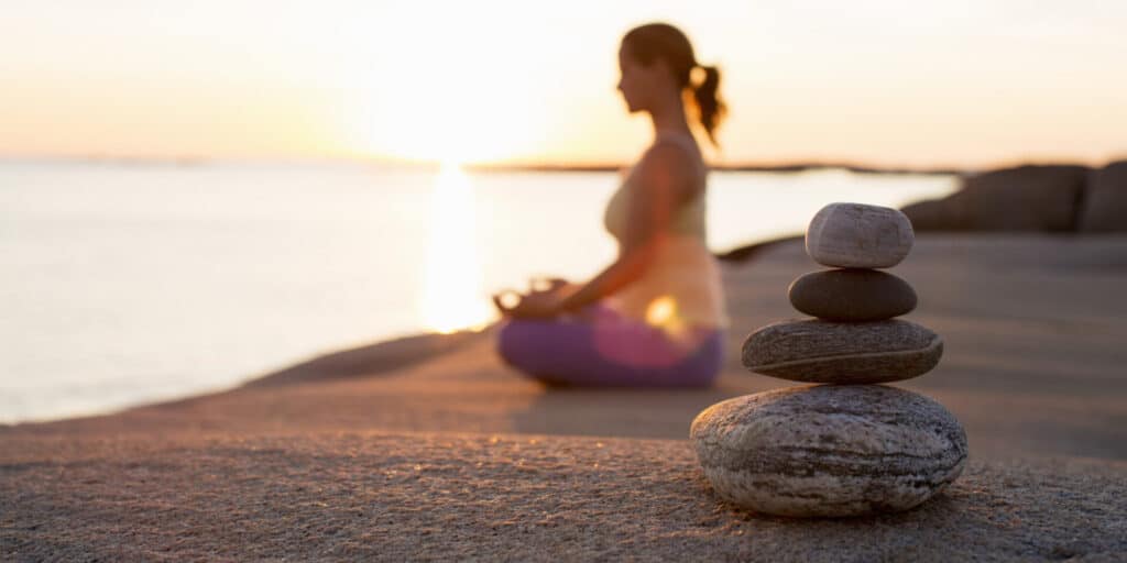 A pregnant woman meditating by the water at sunset.