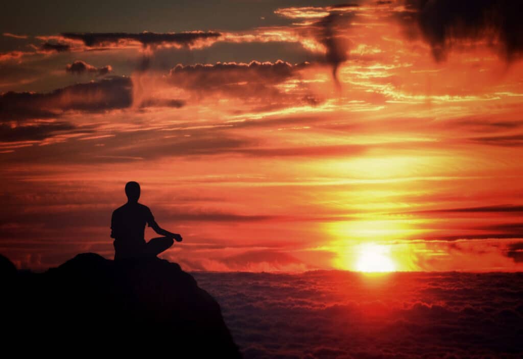 Silhouette of a person meditating at sunset on a mountain.