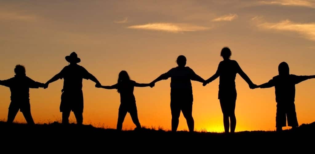 Silhouetted family holding hands at sunset against orange sky.