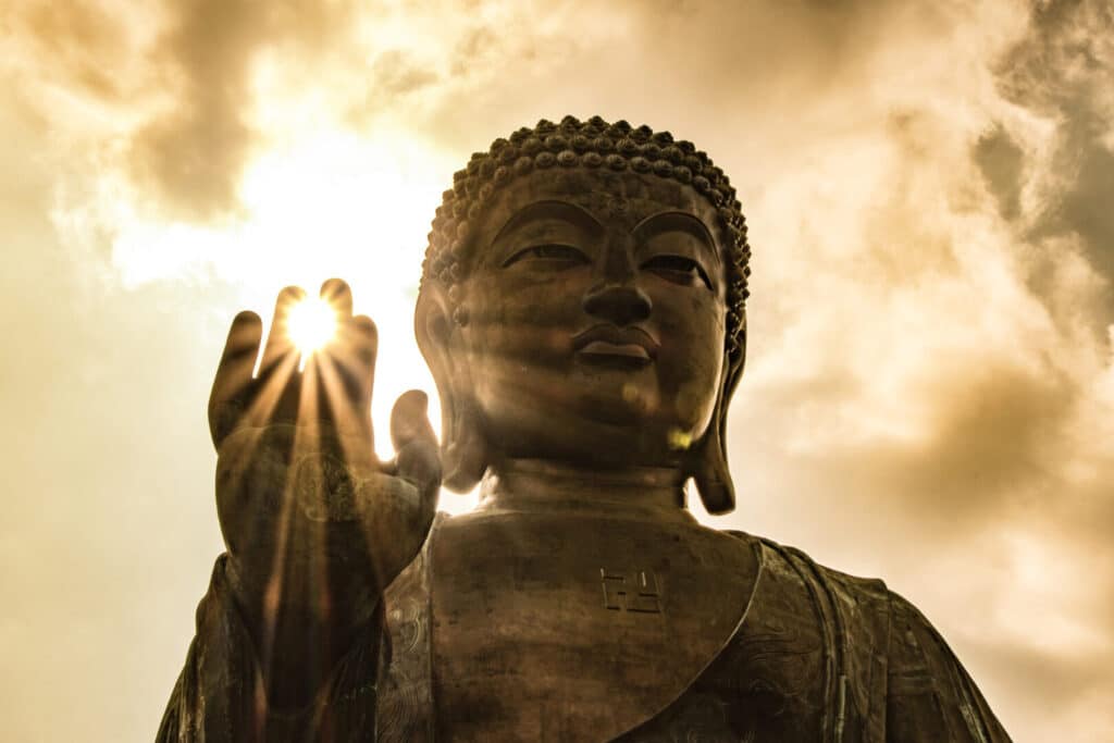 Sun shining through Tian Tan Giant Buddha on hillside in Hong Kong