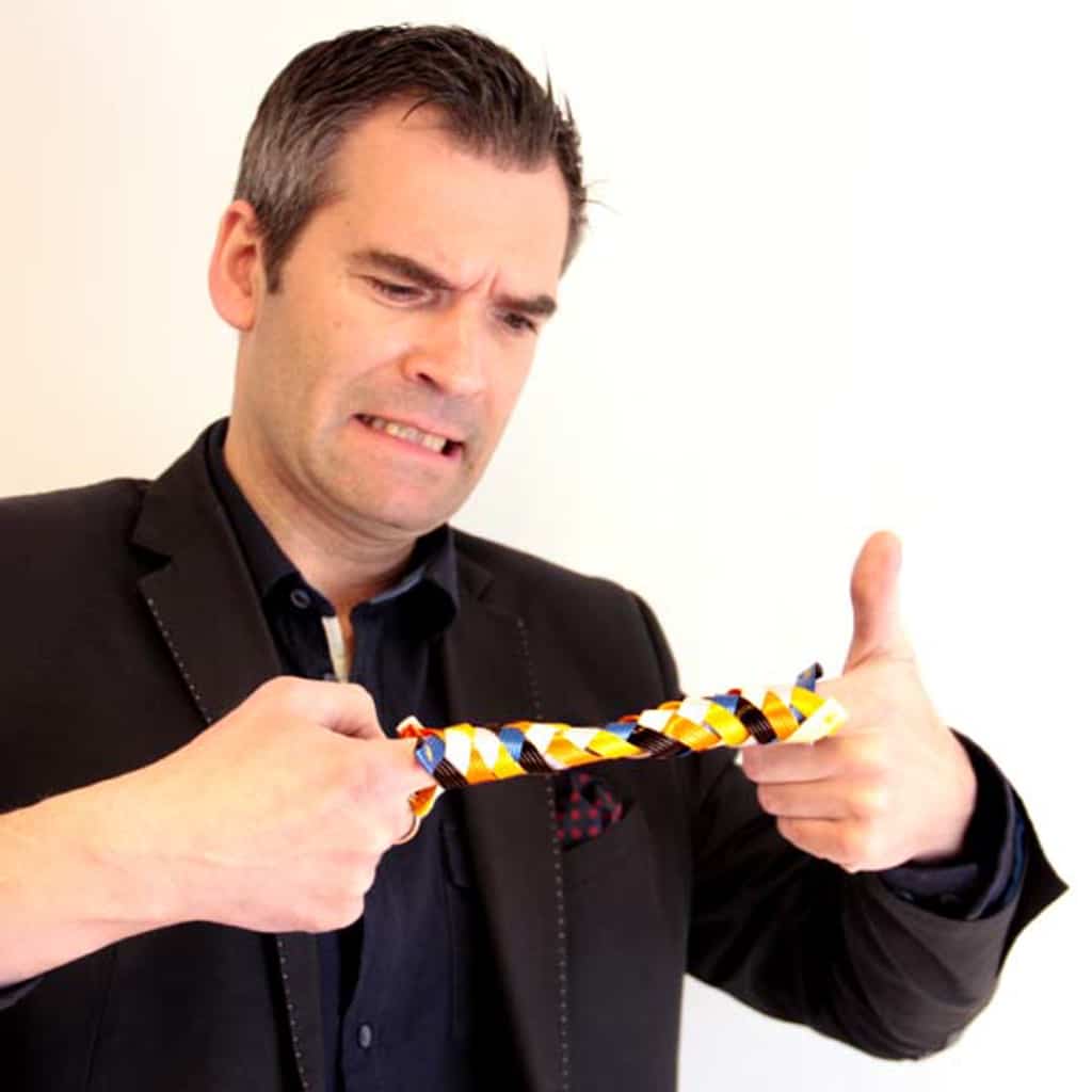 A man struggling to untangle a striped tie with a frustrated expression.