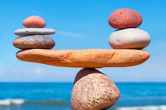 Balanced stones on a wooden plank by the sea under a clear blue sky.