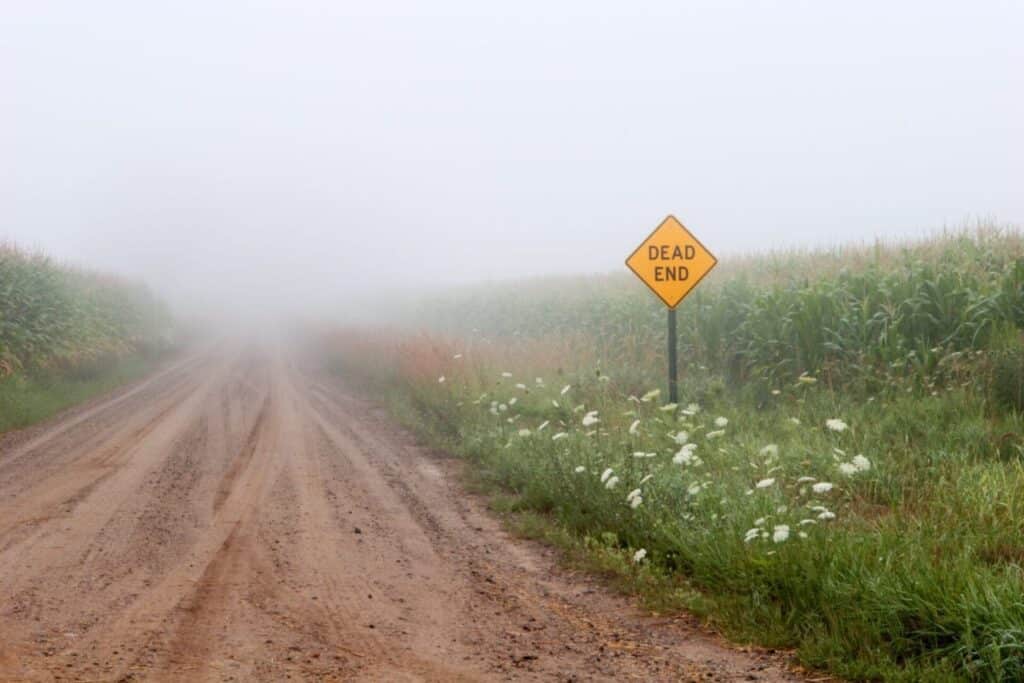A foggy dirt road with a "Dead End" sign on the side.