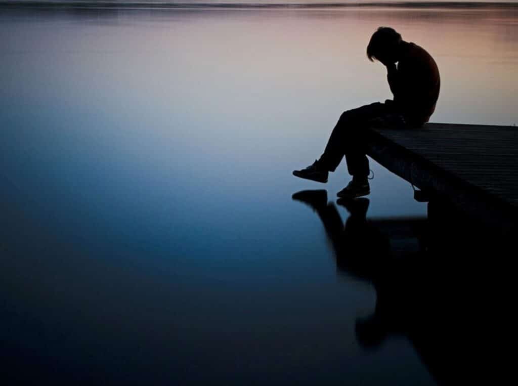 Person sitting alone by calm water at dusk.