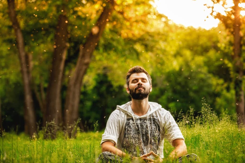 A man meditating outdoors in a green park.