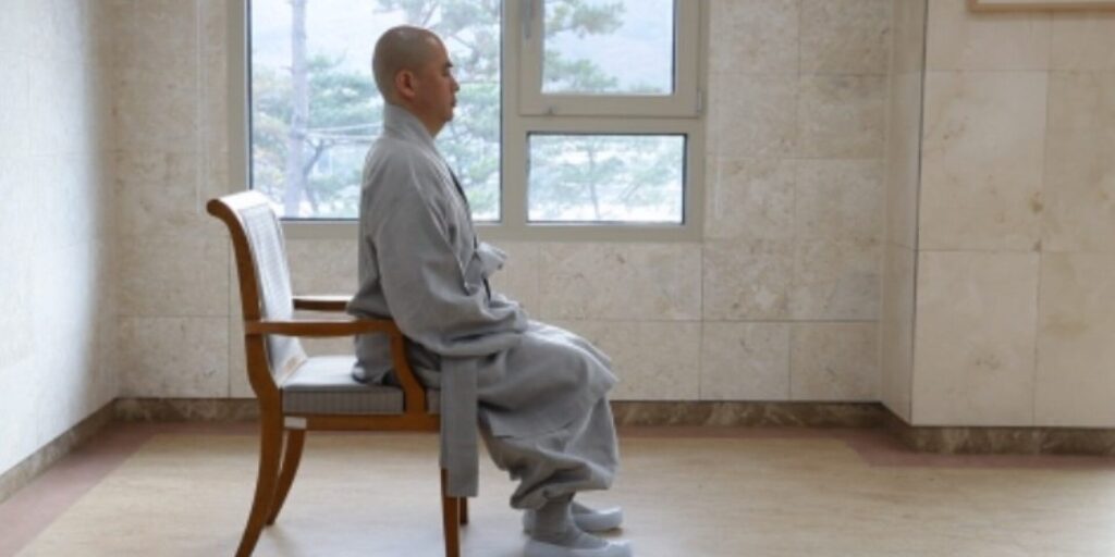 A monk meditating quietly by a window.
