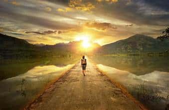 Guy walking on a bridge surrounded by water on both sides as the sunsets.