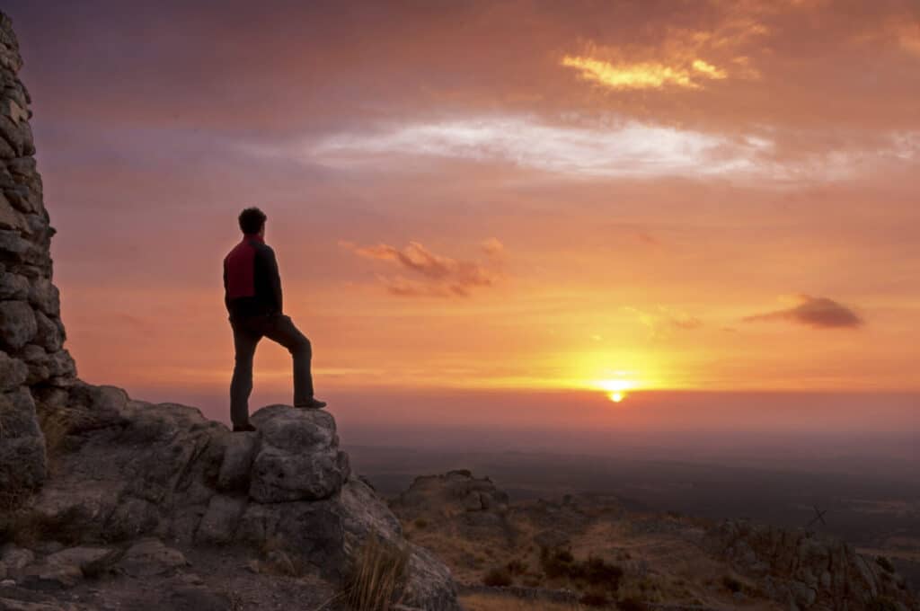 A person standing on a rock watching the sunset.