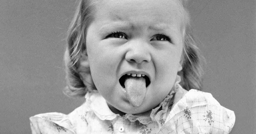 Black and white photo of a child sticking out their tongue.