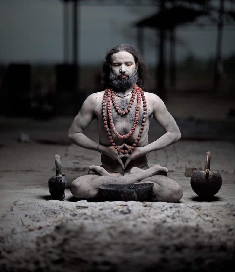 A bearded man meditating in a dimly lit room.
