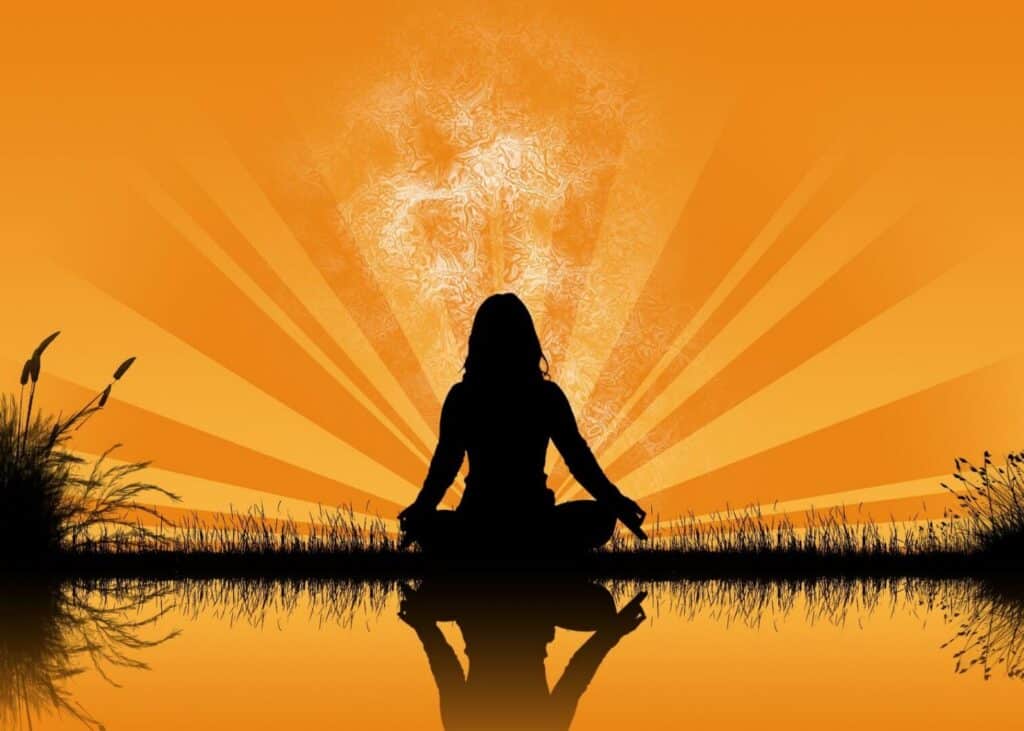 Silhouette of a person meditating against an orange radiant background.