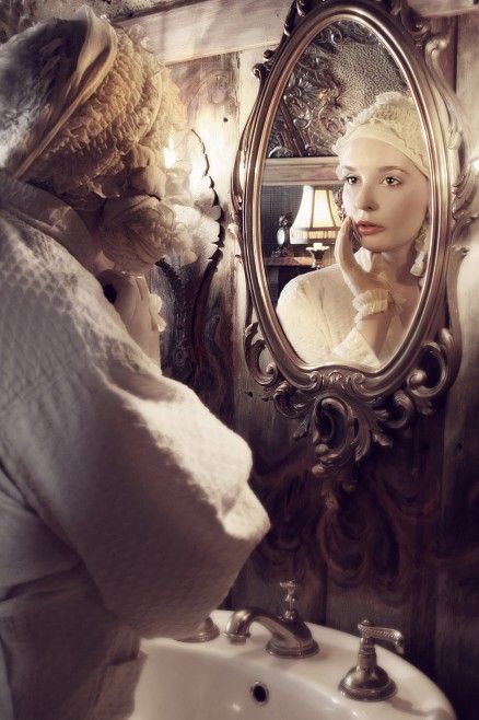 A woman looking at herself in an ornate mirror with a reflective expression.