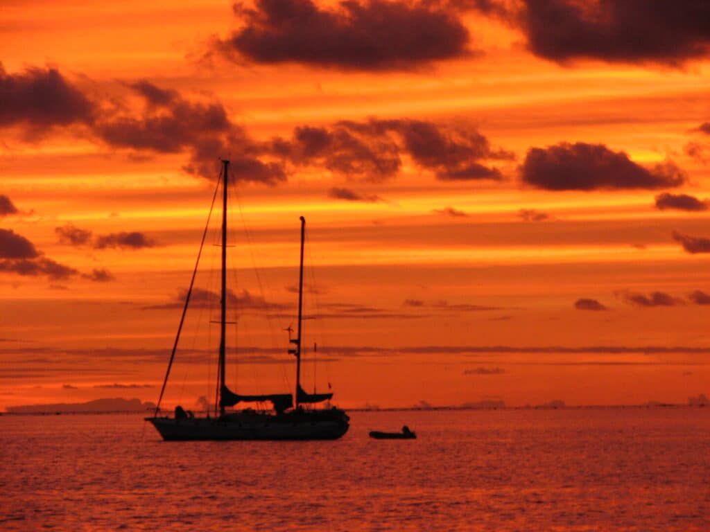 Sailboat on calm water at sunset with vibrant orange sky.