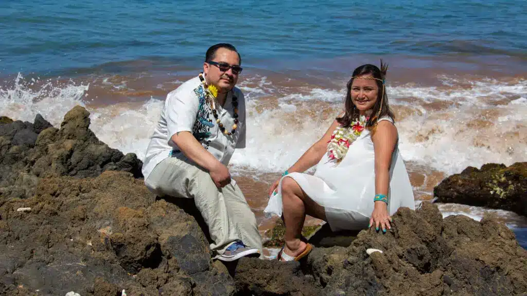 Bride and Groom sitting on rocks with the beach behind them.