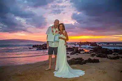 Couple with their marriage certificate on a beach in Maui with the sun setting in the background.