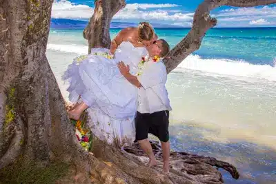 Couple posing for a photo at a beach in Maui, The wife is leaning on the palm tree