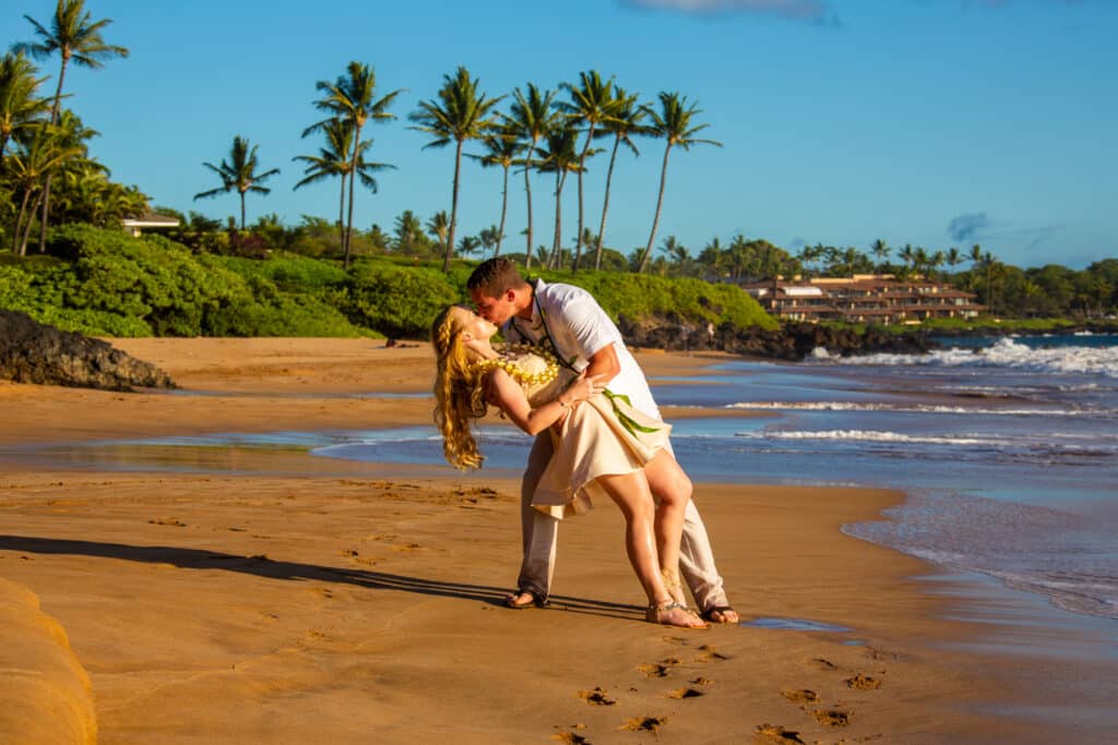 Couple dancing on a sandy beach with palm trees in the background.