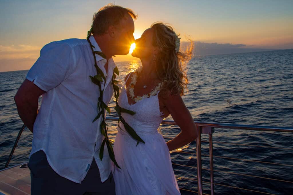 Couple posing for photo on a sailboat with the sunset behind them