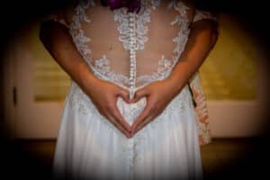 Bride forming a heart with hands over wedding dress back.