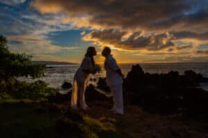 Silhouettes of a couple with a dog at sunset by the water.