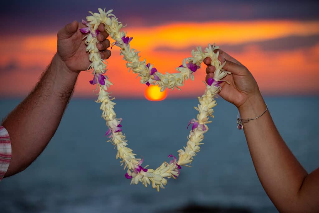 Hands holding lei against sunset backdrop.